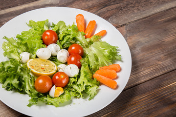 Tasty salad with cherry tomatoes, salad leaves, lemon, spices, carrot and quail eggs on wooden table. Healthy food