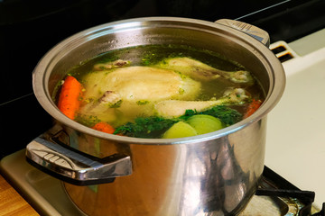 Big chicken is cooked in a saucepan on a gas stove.