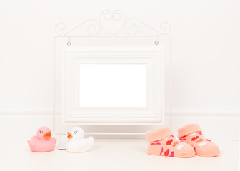Empty white picture frame with space for text or wishes in a white living room setting with pink baby sock and pink and white rubber ducks