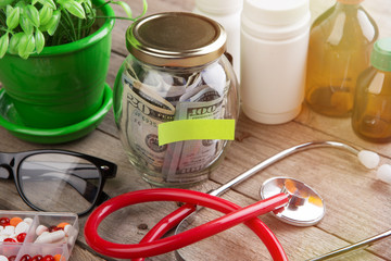 Saving money for health care insurance - money glass, stethoscope, pills and bottles