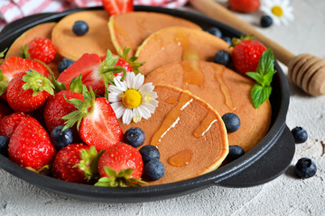 Pancakes with berries and honey in a pan on a concrete background
