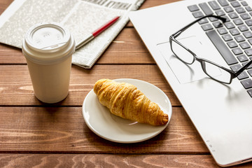 Business lunch with croissant and laptop on wooden desk
