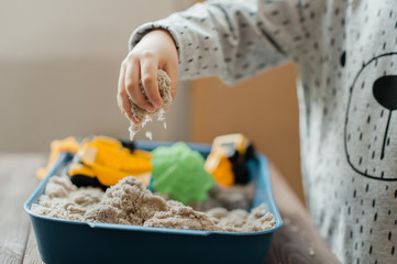 Child playing with kinetic sand and toy construction machinery
