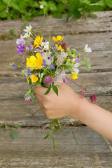 Bouquet of summer wildflowers in hand on a wooden surface background 