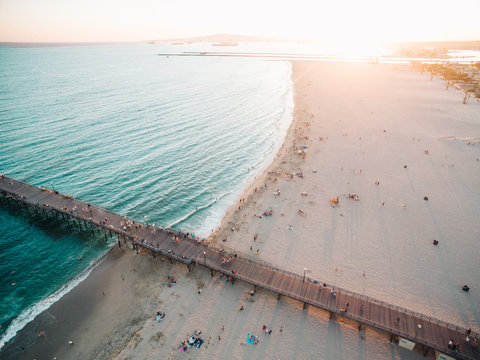 Aerial view of pier in sea with sandy beach at sunset