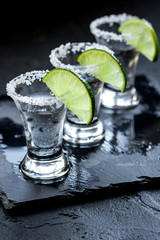 Silver tequila shots with ice and lime on black table background