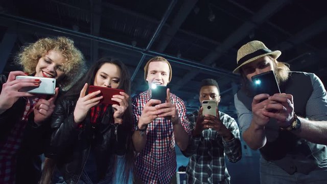 Several young diverse people running to camera and taking many pictures with their smartphones using flashlight