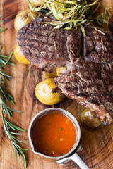 Closeup of delicious grilled beef steak with roasted potatoes and rosemary with tomato hot sauce on a wooden background.