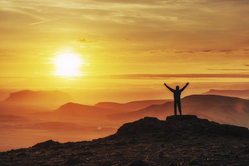 Happy man standing on a cliff at sunset