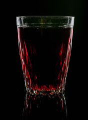 A glass with red drink on a dark background.