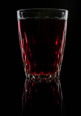 A glass with red drink on a dark background.