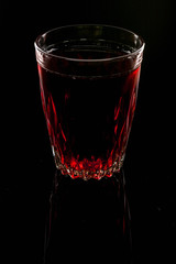 A glass with red drink on a dark background.