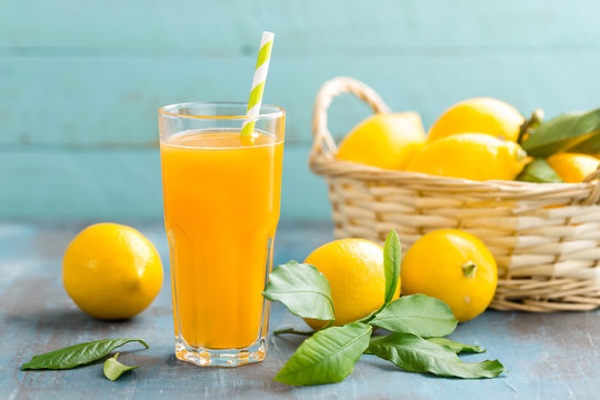Lemon juice in glass and fresh fruits with leaves on wooden background, vitamin drink or cocktail