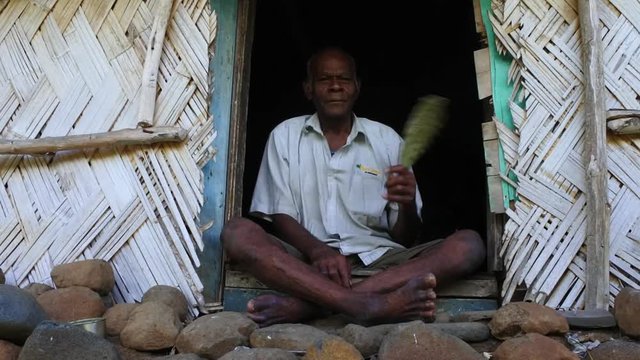 Elderly indigenous Fijian man sit outside his village bure home