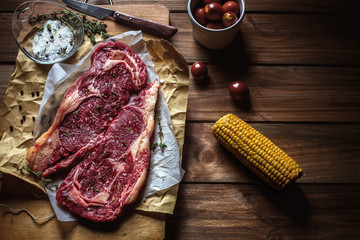 Raw beef steak with corn, tomatoes and spiced salt over a wooden table.