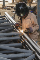 Worker with safety equipments and protective mask welding steel structure in construction factory -...