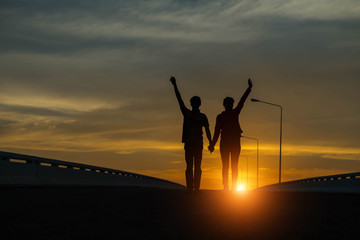 Young couple hand up at sunset on the road.