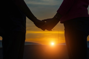 Closeup of loving couple holding hands while walking at sunset