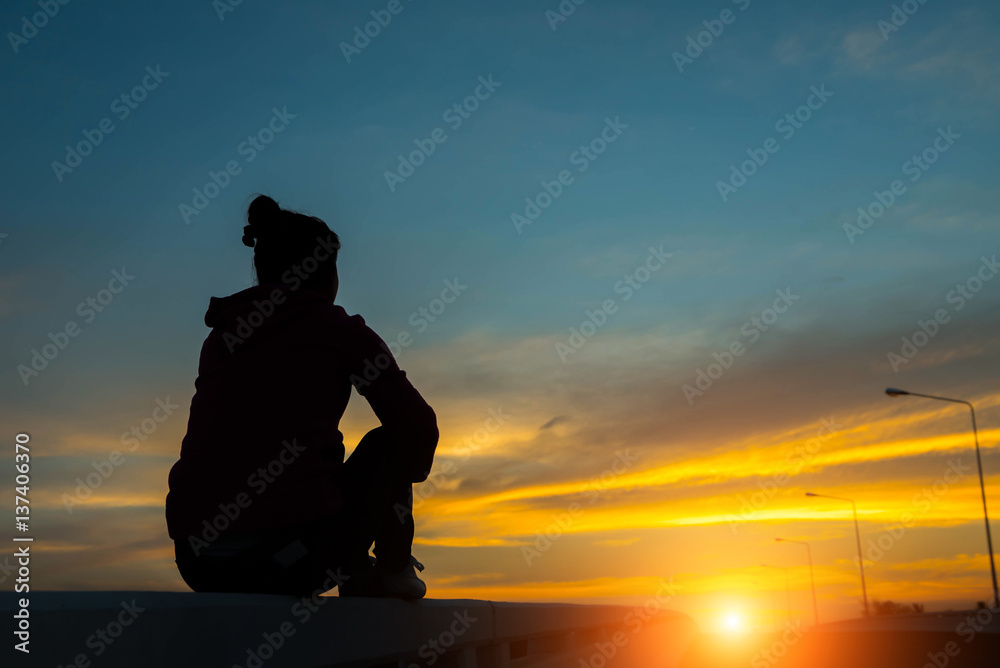 Wall mural silhouette woman on road watching yellow and orange setting sun at sunset