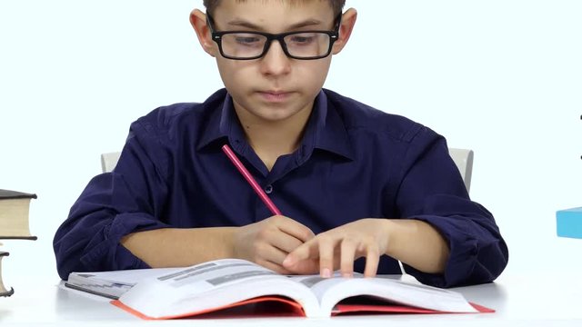Boy sits at a table recording something into her notebook and flips through the book. White background