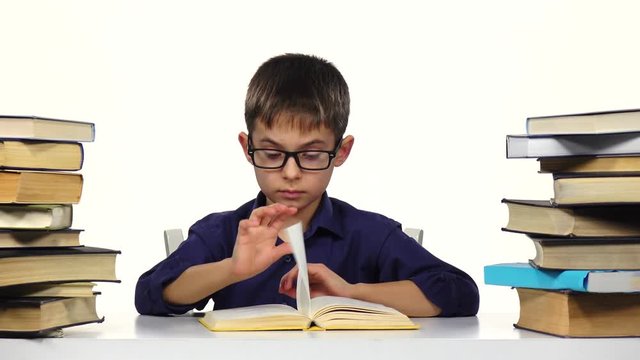 Little boy sits at a table and reads the book slowly. White background