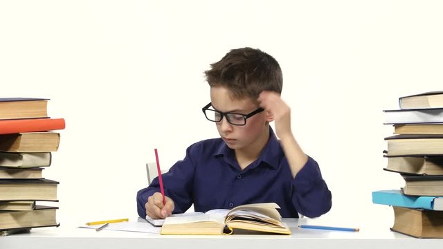 Boy sits at a table recording something into her notebook and flips through the book. White background