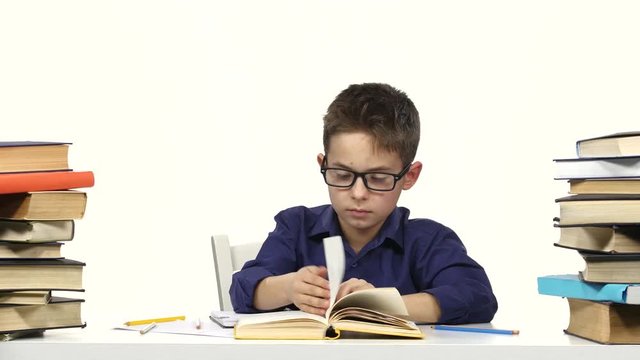 Little boy sits at a table and reads the book slowly. White background