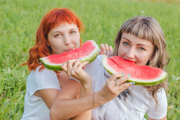 Две девушки на природе едят арбуз.
