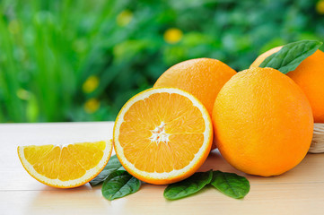 Orange, half of orange, orange lobule and basket with oranges on the wooden table on the green blurred background