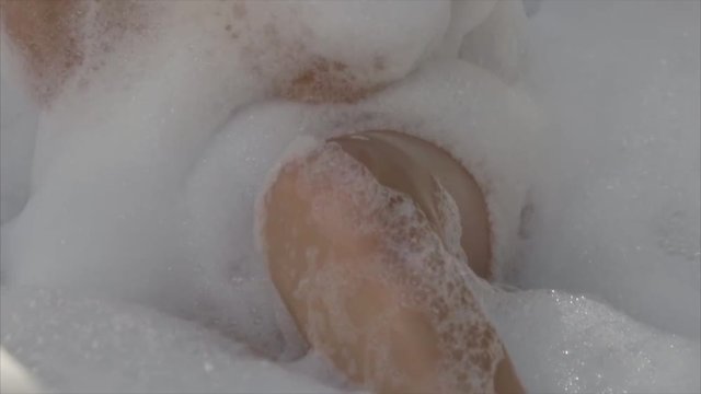 Blonde woman relaxing in an open bath with foam, skin care, luxurious lifestyle.