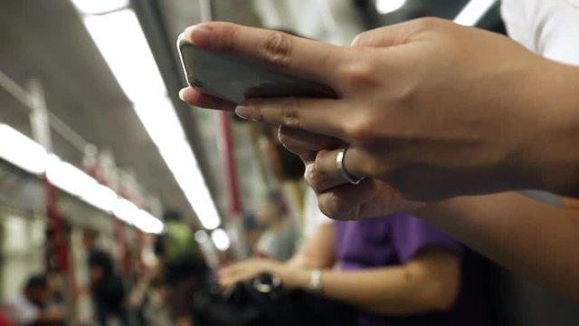 Asian young woman sit down in a train checks her phone, and writting SMS text with her friends using Line, social network, as she waits for arrive her stop station in Hong Kong-Dan
