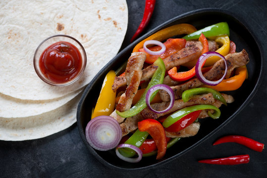 Frying pan with tex-mex pork fajitas and tortillas, above view