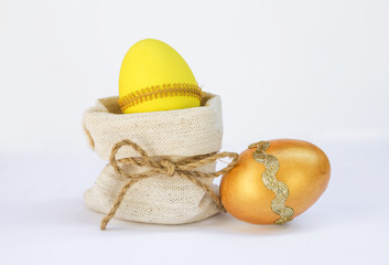 Yellow Easter egg in canvas bag and golden egg on white background