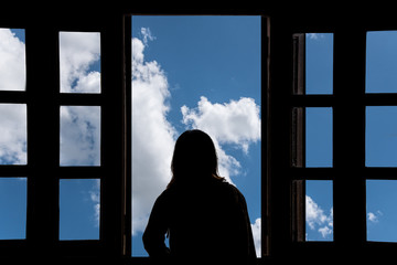 Silhouette young woman in the hotel, looking blue sky through the window