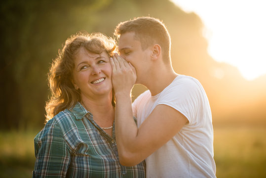 Son whispering a secret into mother's ear