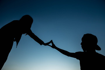 Concept or conceptual heart shape or symbol made of human or woman and man hand silhouette over a...
