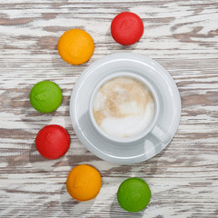 Macarons and a cup of cappuccino on wooden background. Conceptual, closeup.