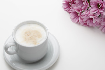 Flowers and a cup of cappuccino on white background. Conceptual, closeup.
