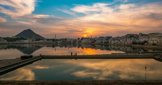 Sunset to twilight time lapse at Pushkar, Rajasthan, India. Stunning colorful sky and moving clouds over temples, buildings and ghats reflecting on the holy water of the lake.