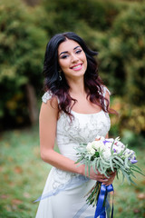 Brunette bride holds wedding bouquet with greenery posing outside