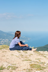 Naklejka na ściany i meble Young woman relaxing on a rock and enjoying the beauty of seascape sitiing on the mountain top. Travel, Healthy Lifestyle concept