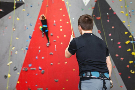 Coach climber belay amateur athlete on a high climbing wall.