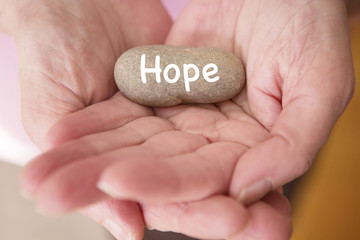 closeup of womans hands holding stone with the word hope