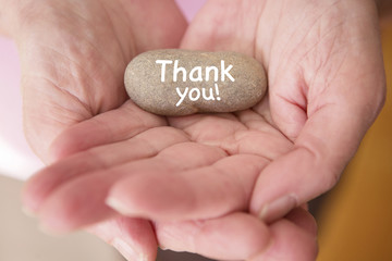 closeup of womans hands holding stone with words thank you