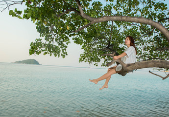 Obraz premium young woman sitting back on tree with the sea