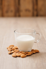 Glass of almond milk with almonds on wooden table