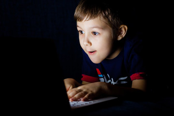 Little boy playing on laptop at the game at night in the dark.