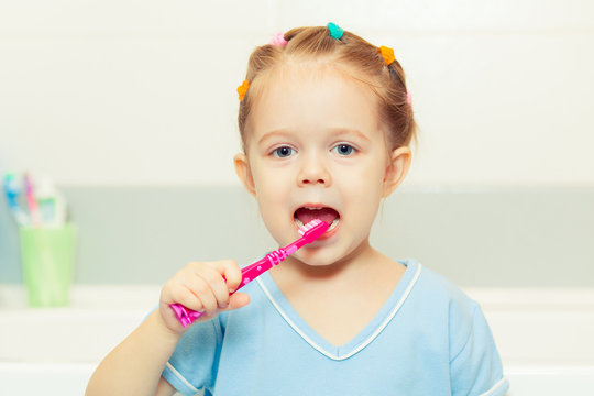 Little girl brushing her teeth in the bathroom. Smiling child holding a toothbrush.