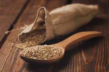 Healthy buckwheat grain in a linen bag and wooden spoon on light background, selective focus. Organic and nutritious meal, gluten free