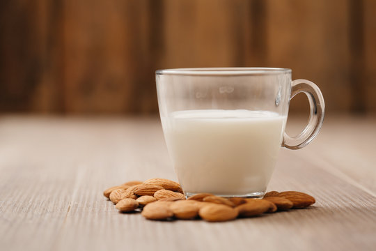 Glass of almond milk with almonds on wooden table